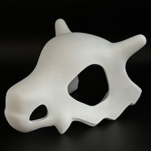 Könnte beinhalten: Weiße Plastikmaske in Schädelform mit einem großen Augenloch und kleineren Löchern für Nase und Mund.