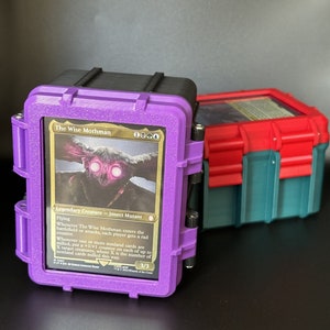 Pode incluir: Uma caixa de cartas roxa e preta com um cartão Magic: The Gathering com borda dourada dentro. O cartão mostra uma criatura com olhos vermelhos brilhantes e o texto "The Wise Mothman".