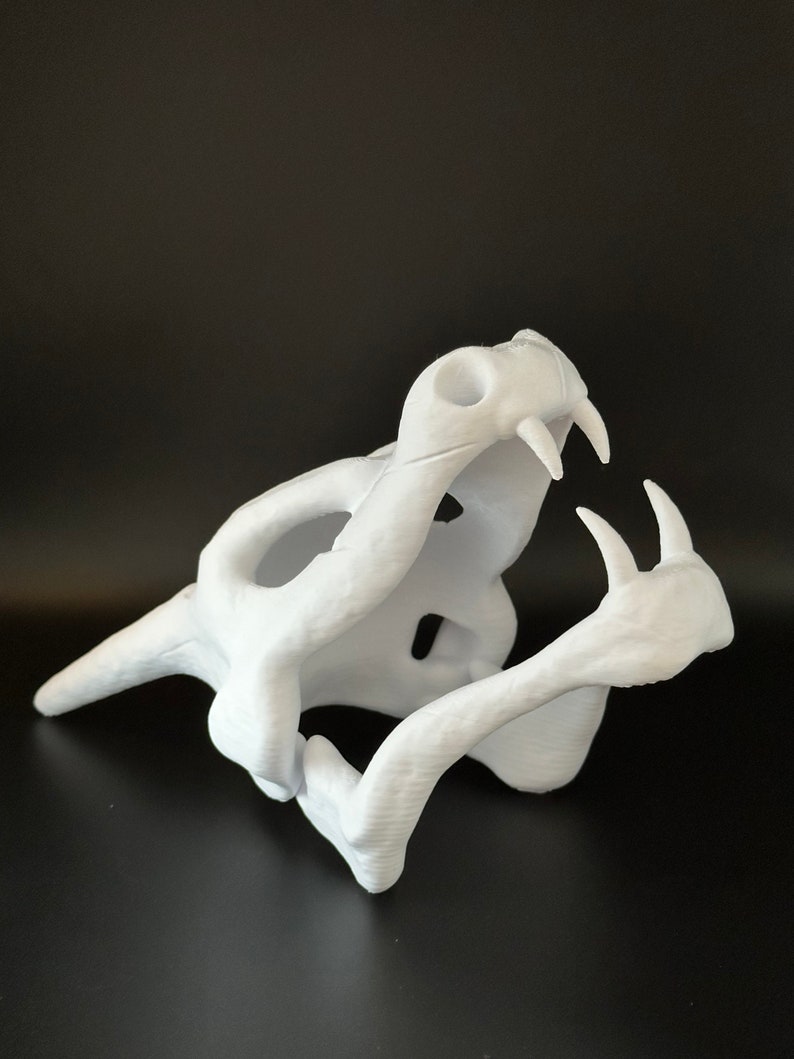 May include: White 3D printed model of a snake skull with its jaw open. The skull is detailed with teeth and bone structure.