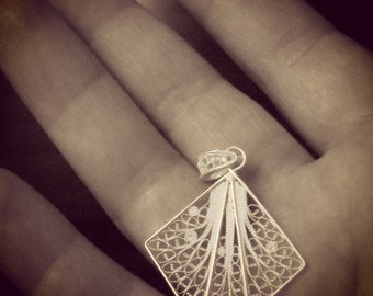 May include: A silver filigree pendant with a geometric design. The pendant is intricate and delicate, with a fan-like shape.