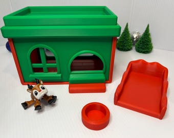 May include: A red and green toy house with a matching slide and a small red circular piece. A brown and white reindeer figurine is in front of the house. Two small green Christmas trees are in the background.