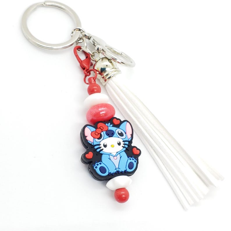 May include: A blue and white cartoon character keychain with red hearts and a white tassel. The keychain has red and white beads.