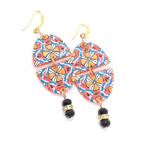 May include: Dangle earrings featuring two stacked semi-circular segments with a vibrant orange, pink, and blue floral pattern. Each earring is finished with a dangling black faceted bead accented by a small silver-toned rhinestone spacer ring.