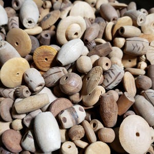 May include: A large collection of wooden beads in various shapes, sizes, and colors. The beads are mostly brown and beige, with some having a natural wood finish and others painted with white or black stripes.