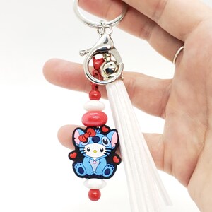 May include: Blue Stitch character keychain with red hearts, red and white beads, and a white tassel. The keychain has a silver metal clasp.