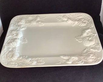 May include: A rectangular, off-white serving platter with raised pumpkin and leaf designs around the edges. The platter has a smooth, flat surface in the center, perfect for displaying food. The pumpkin and leaf design adds a seasonal touch.