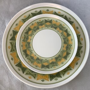 Op de afbeelding: Een set van drie witte keramische borden met een geometrisch patroon in groen en goud. De borden zijn in elkaar genest.