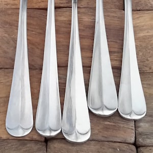 May include: Five silver utensils, including a spoon, a melon baller, a fork, and two teaspoons, are arranged on a wooden surface.