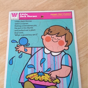 May include: A frame-tray puzzle featuring a cartoon illustration of Little Jack Horner sitting in a corner eating a Christmas pie. The puzzle pieces are shaped like the characters and objects in the illustration. The text on the puzzle reads: "Little Jack Horner sat in a corner Eating a Christmas pie; He put in his thumb and pulled out a plum And said, "What a good boy am I!"  Frame-Tray Puzzle Develops Coordination & Motor Control"