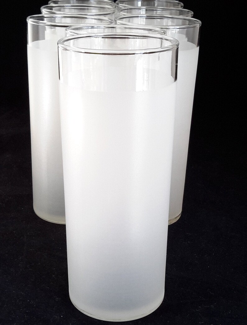 May include: Set of six frosted glass tumblers. The glasses are tall and cylindrical with a slightly rounded bottom. They are made of clear glass that has been frosted to give them a white, opaque appearance.