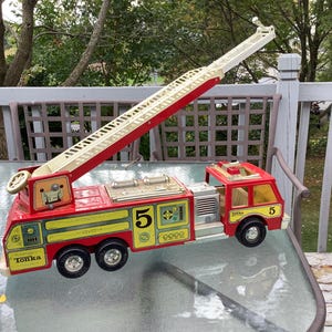 May include: A vintage red and yellow Tonka fire truck toy with a white extending ladder. The toy truck has black wheels, the number 5 on the side, and the Tonka logo. The ladder extends to a significant height.