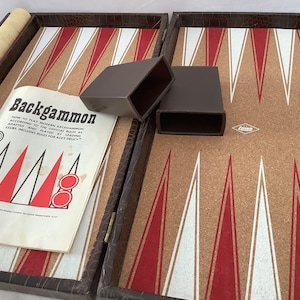 May include: A vintage backgammon set with a brown faux-leather exterior. The game board features a cork-like surface with red and white triangles. Includes dice cups, dice, and a rule book. The text on the rule book reads "Backgammon".
