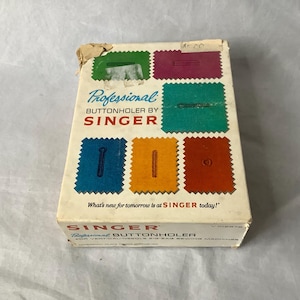 Op de afbeelding: Een witte doos met een blauw en rood Singer-logo. De doos is voor een professionele knoopsgatnaaier voor verticale naaimachines en zigzagnaaimachines. De doos heeft een afbeelding van een knoopsgat met verschillende steekpatronen.