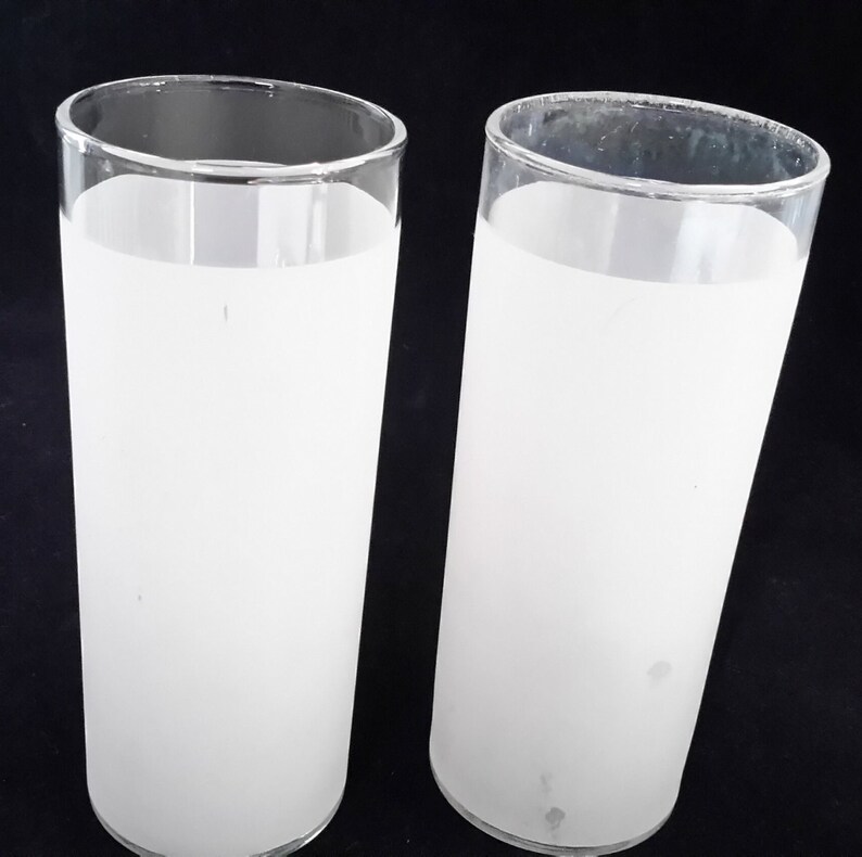 May include: Two frosted glass tumblers with a white frosted finish. The glasses are clear and cylindrical in shape.