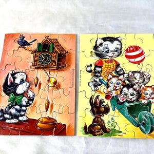 May include: Two rectangular jigsaw puzzles featuring illustrated scenes. The left puzzle shows a black and white kitten with a green bow near a cuckoo clock. The right puzzle depicts a black and white kitten pushing a wheelbarrow with three smaller kittens and a dog.