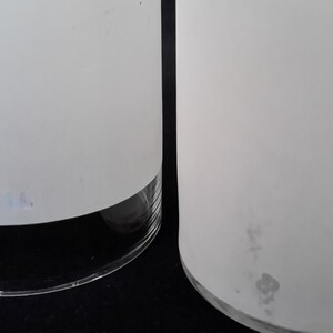 May include: Two white frosted glass cylinder vases with a clear glass base. The vase on the right has a few small dark spots on the frosted surface.