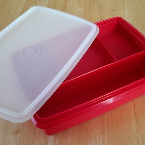 Puede incluir: Un contenedor de almacenamiento de plástico rojo con una tapa blanca. El contenedor tiene tres compartimentos y es ideal para organizar artículos pequeños.