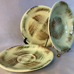 Può includere: Tre piatti in ceramica con un design a pennellate verdi e marroni. I piatti sono impilati su un supporto in metallo.