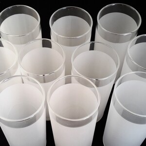 May include: Set of ten frosted glass tumblers with a silver rim. The glasses are all empty and arranged in a circle on a black background.