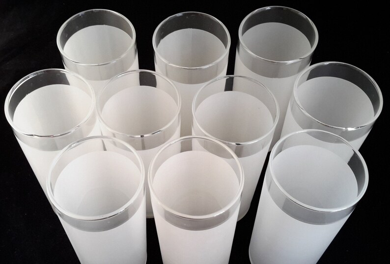 May include: Set of ten frosted glass tumblers with a silver rim. The glasses are all empty and arranged in a circle on a black background.