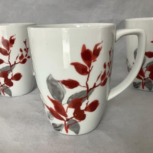 May include: White ceramic mugs with a red and gray floral design. The mugs have a curved shape and a handle. The floral design features red leaves and gray leaves on a white background. The mugs are suitable for coffee, tea, or other beverages.