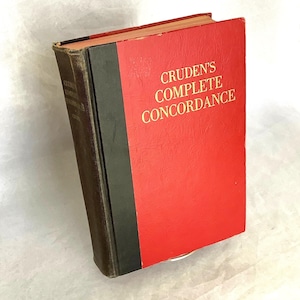 May include: A vintage book titled "Cruden's Complete Concordance." The book has a red cover with gold lettering and a black spine. The edges of the book show signs of wear, indicating its age. The book is slightly angled, showcasing its cover and spine.