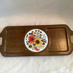 May include: A wooden serving tray with three compartments. The centre compartment features a white ceramic tile with a colourful floral design. The tray has two handles on the sides.