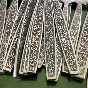 May include: A close-up of a set of cutlery with floral patterns etched into the handles. The cutlery is made of stainless steel and has a polished finish.