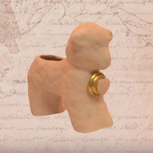 Könnte beinhalten: Ein hellbrauner Keramik-Pflanztopf in Form eines stehenden Lamms mit einem goldenen Ring um den Hals. Der Topf hat eine herzförmige Öffnung an der Seite.