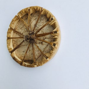 May include: A round, tan-colored Native American hand drum with a leather covering and a woven design. The drum is made of wood and has a natural, rustic look.
