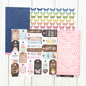 Puede incluir: Un conjunto de 10 hojas de papel para scrapbooking con varios patrones, incluyendo mariposas, lunares y diseños florales. Las hojas de papel son en tonos de rosa, azul y verde. El conjunto también incluye una hoja de etiquetas con varios mensajes, como "Happy Day", "Sweet Treat" y "Thinking of You".