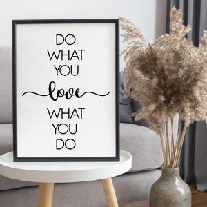 May include: A framed print with the text "DO WHAT YOU LOVE WHAT YOU DO" in black on a white background. The word "love" is written in a cursive font. The frame is black, and the print is displayed on a white table.