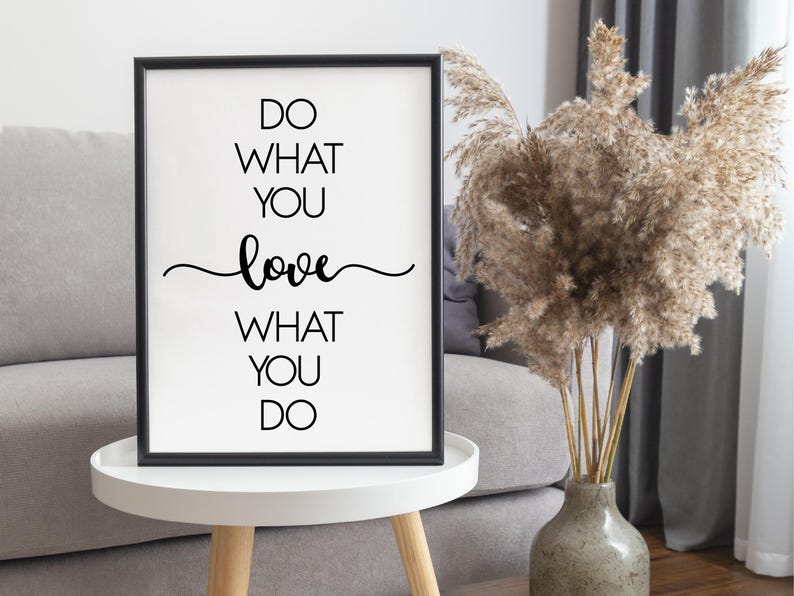 May include: A framed print with the text "DO WHAT YOU LOVE WHAT YOU DO" in black on a white background. The word "love" is written in a cursive font. The frame is black, and the print is displayed on a white table.