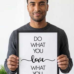 May include: A framed print with the words "DO WHAT YOU love WHAT YOU DO" in black script. The frame is black, and the background is white. The print is held by a person wearing a gray sweater.