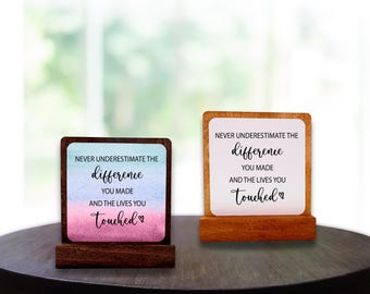 May include: Two wooden desk signs. Each sign displays the text "Never underestimate the difference you made and the lives you touched." One has a blue, pink, and white watercolor background, the other a white background.