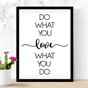May include: A framed print with the text "DO WHAT YOU love WHAT YOU DO" in black against a white background. The frame is black. A small white vase with pink flowers sits in front of the print.