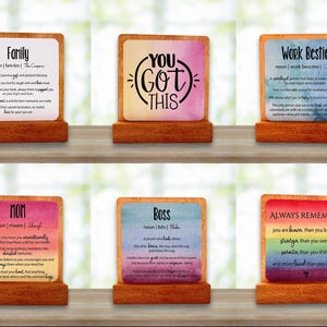 May include: Six wooden plaques with motivational messages. Each plaque has a colourful background and text, including phrases such as "Family," "You Got This," and "Work Bestie." The plaques are displayed on a wooden surface.