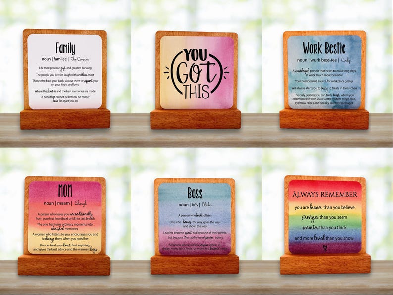 May include: Six wooden plaques with motivational messages. Each plaque has a colourful background and text, including phrases such as "Family," "You Got This," and "Work Bestie." The plaques are displayed on a wooden surface.