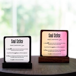 May include: Two wooden plaques with the words "Soul Sister" and a definition. One has a black base, the other a brown base. The text is black, with a definition of "Soul Sister". The background of one plaque is pink and yellow.