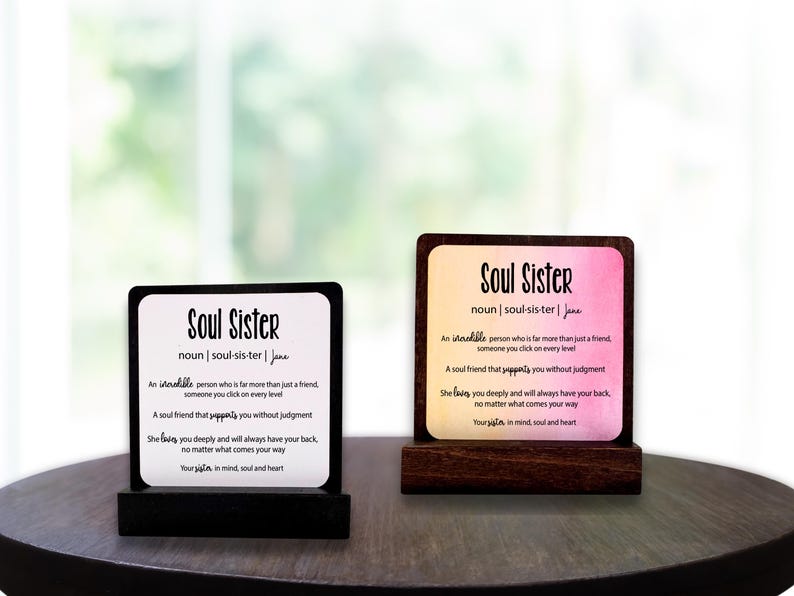 May include: Two wooden plaques with the words "Soul Sister" and a definition. One has a black base, the other a brown base. The text is black, with a definition of "Soul Sister". The background of one plaque is pink and yellow.