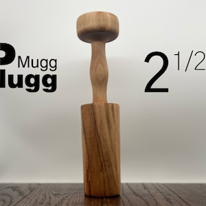 May include: A wooden kitchen tool, a 2 1/2 inch muddler, with a round top and a handle. The muddler is made of light brown wood with darker brown wood grain.