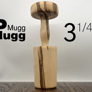 May include: A wooden mugg with a 3 1/4" diameter. The mugg is made of light wood with dark brown streaks. The mugg has a round top and a cylindrical base.