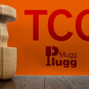 May include: A wooden mortar and pestle set on a wooden surface. The mortar is a light brown color and the pestle is a darker brown color. The background is a bright orange color with the text "TCC Mugg Ilugg" in red.