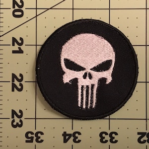 May include: A black and white embroidered patch featuring the Punisher skull logo. The skull is white with black eyes and a black jawline. The patch is circular and has a black border.