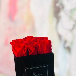 May include: A black velvet box with a red rose arrangement. The box has a silver label that reads "Boutique Rouge".
