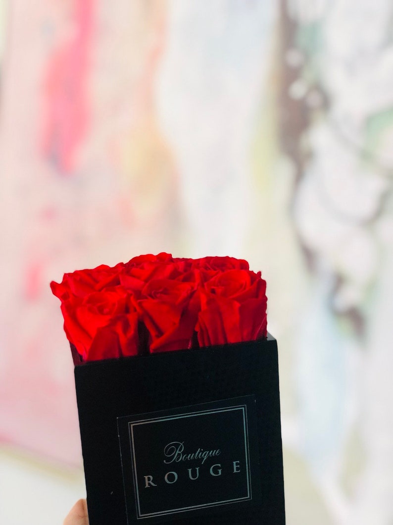 May include: A black velvet box with a red rose arrangement. The box has a silver label that reads "Boutique Rouge".