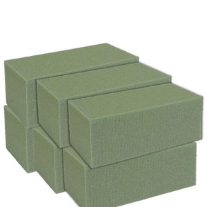May include: A stack of six green floral foam bricks. The bricks are rectangular and have a slightly textured surface.
