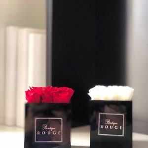 May include: Two black square boxes with red and white roses inside. The boxes have a gold label that says "Boutique Rouge".