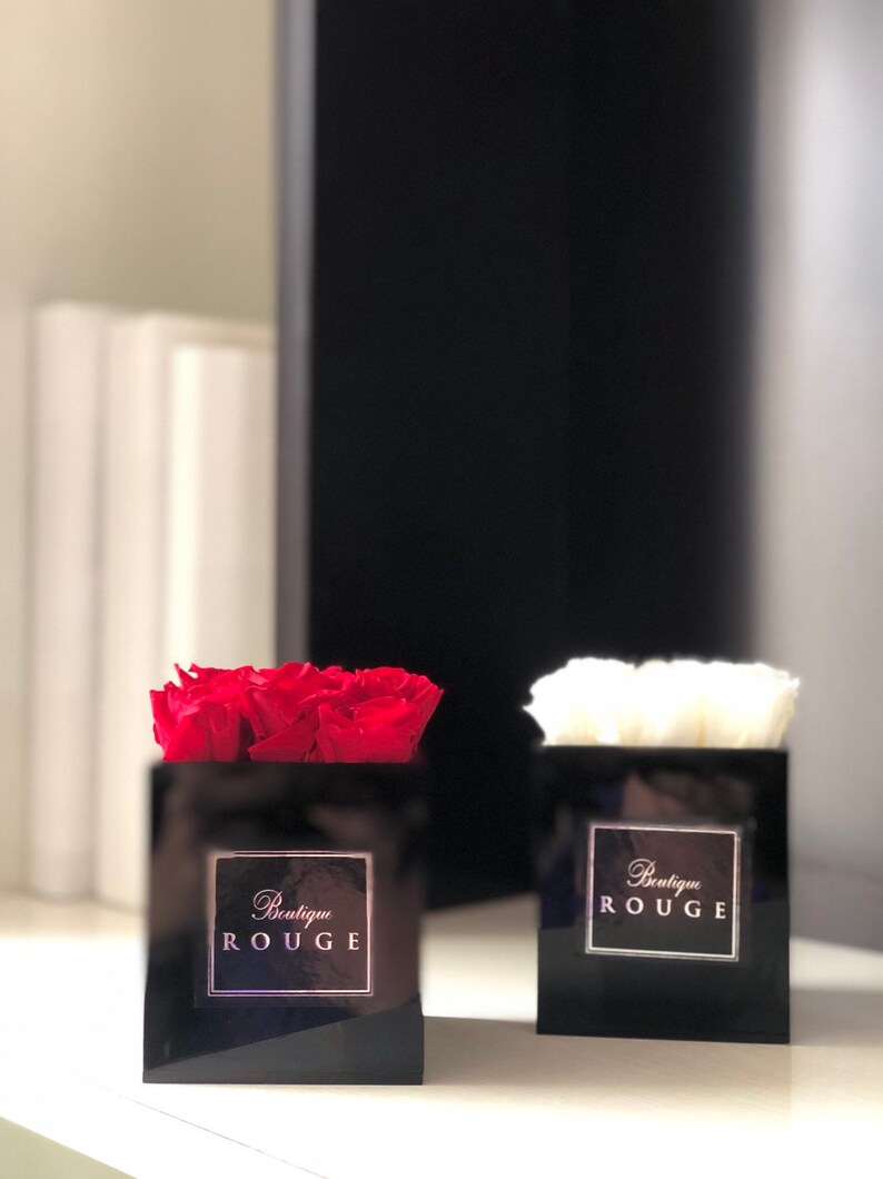May include: Two black square boxes with red and white roses inside. The boxes have a gold label that says "Boutique Rouge".