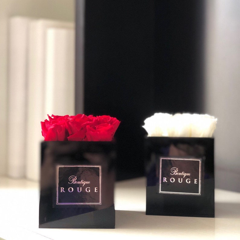 May include: Two black square boxes with red and white roses inside. The boxes have a gold logo that says "Boutique Rouge".